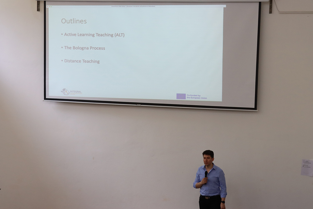 Man with a microphone in front of a slide presentations