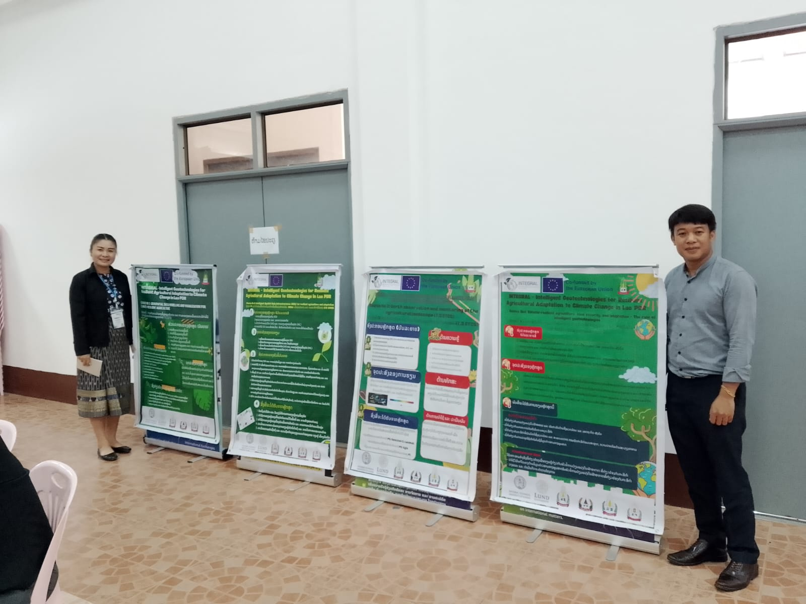 A series of posters and a woman and a man standing on each side, smiling